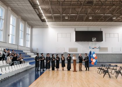 A graduation ceremony held in an indoor gymnasium with graduates and an audience.